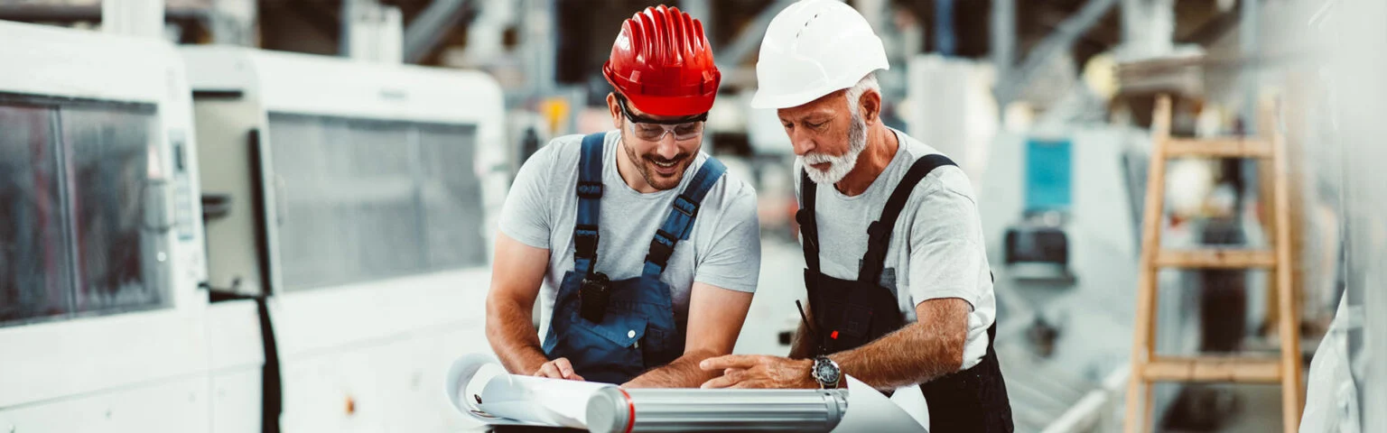 Zwei Männer mit Schutzhelmen arbeiten an einem Bauplan