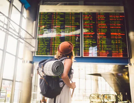 Backpackerin im Bahnhof vor dem Zugfahrplan