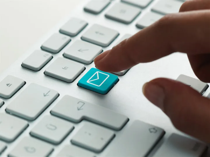 Eine Person drückt auf einen blauen E-Mail-Button auf einer Computertastatur