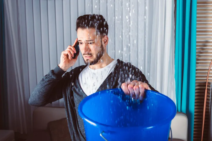 Man hält einen Eimer unter tropfendes Wasser und telefoniert